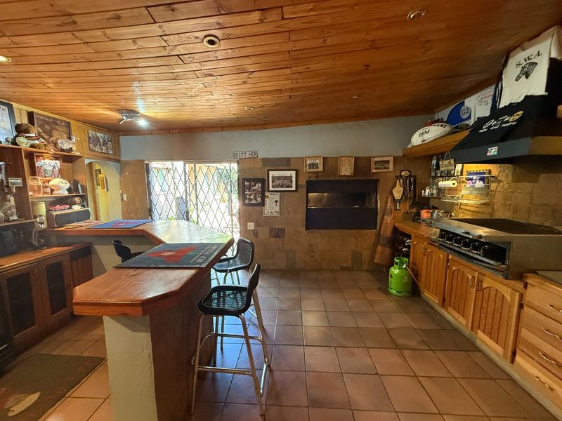 Spacious entertainment bar area featuring a built-in braai, wooden ceiling, tiled flooring, and custom bar counter, ideal for hosting and social gatherings.