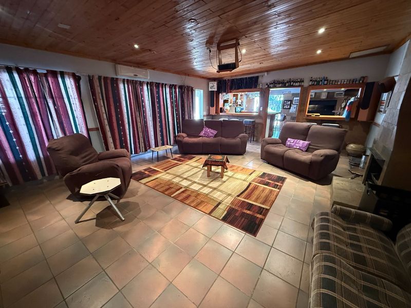 Spacious living room featuring a timber ceiling, tiled flooring, a built-in bar area, and a stone fireplace, offering a comfortable and functional entertainment space.