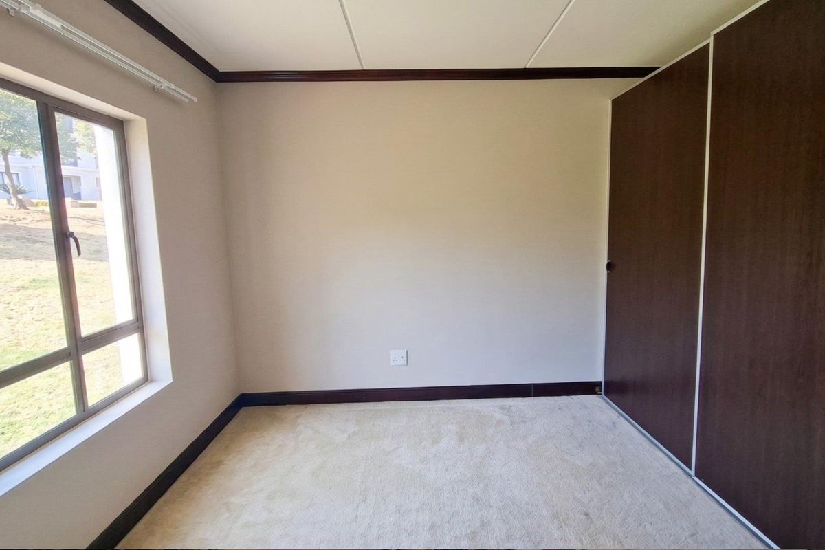 A bright, empty bedroom featuring neutral carpeting, built-in cupboards, and a large window providing natural light and exterior views.