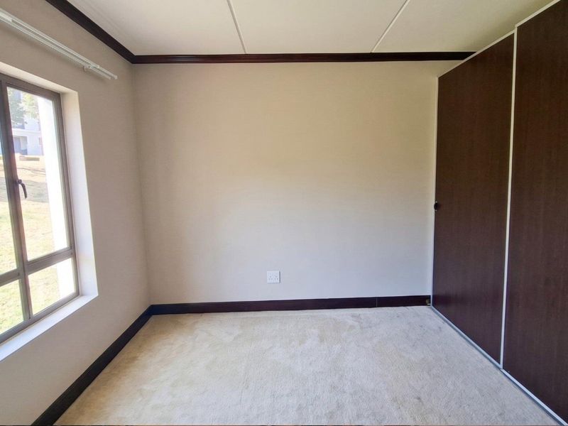 A bright, empty bedroom featuring neutral carpeting, built-in cupboards, and a large window providing natural light and exterior views.