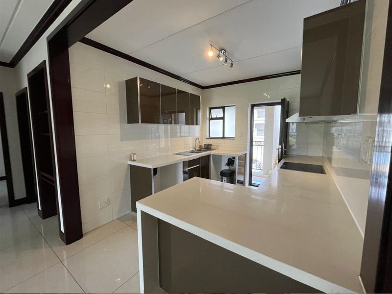 Modern kitchen featuring sleek built-in cabinetry, stone countertops, a hob, and tiled finishes, offering a clean and functional workspace.
