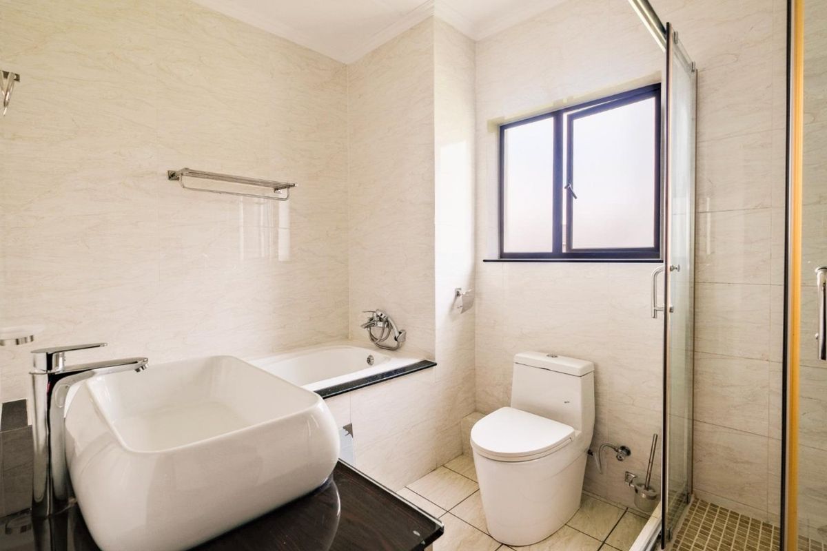 A modern, well-maintained bathroom featuring a vessel sink, built-in bathtub, and a separate glass-enclosed shower with neutral wall and floor tiling.