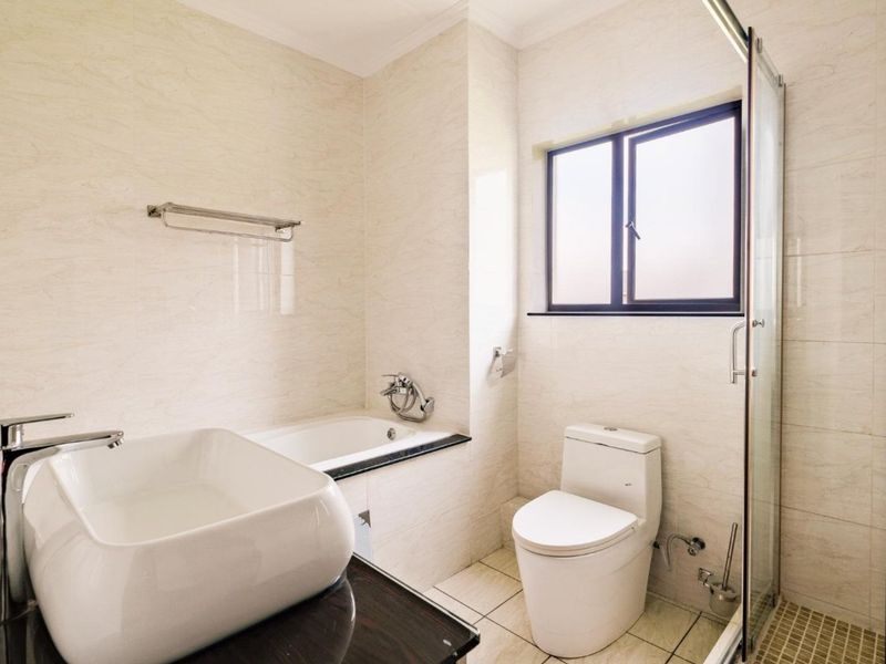 A modern, well-maintained bathroom featuring a vessel sink, built-in bathtub, and a separate glass-enclosed shower with neutral wall and floor tiling.