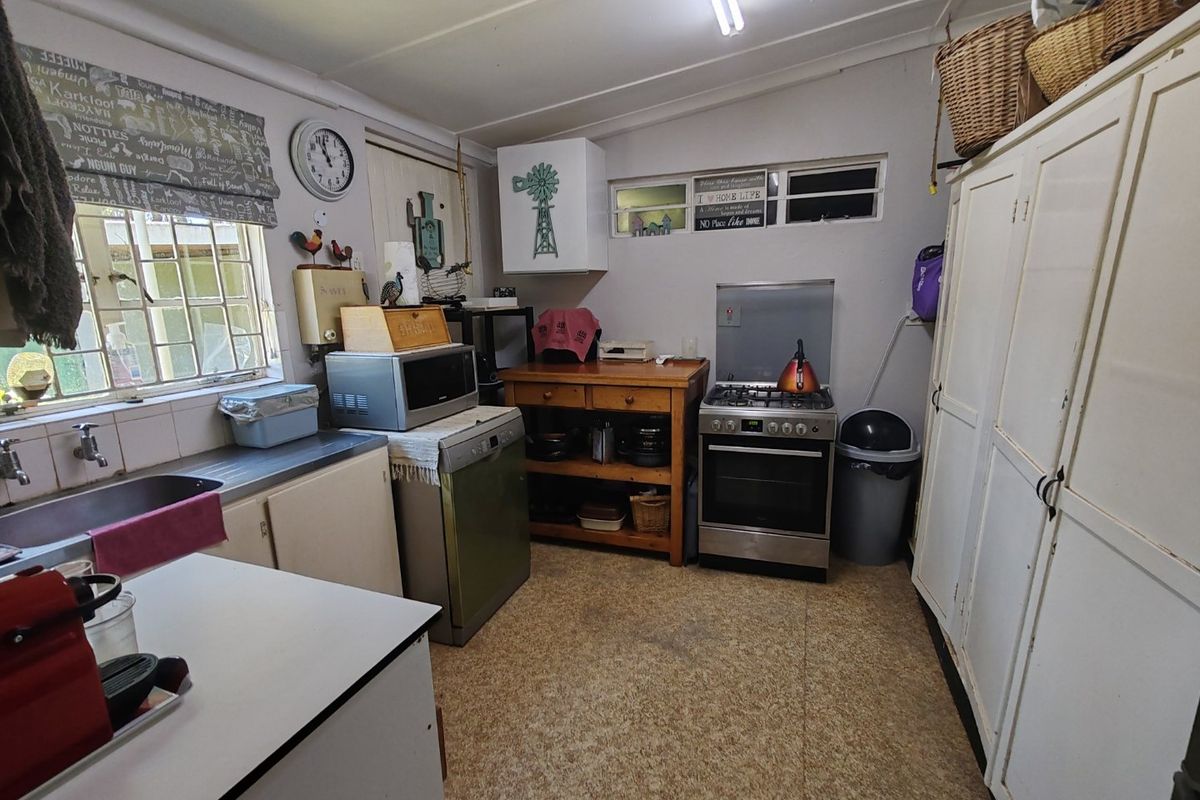 A functional kitchen featuring a freestanding gas stove, stainless steel sink, and built-in storage cupboards, offering potential for modernization and aesthetic updates.