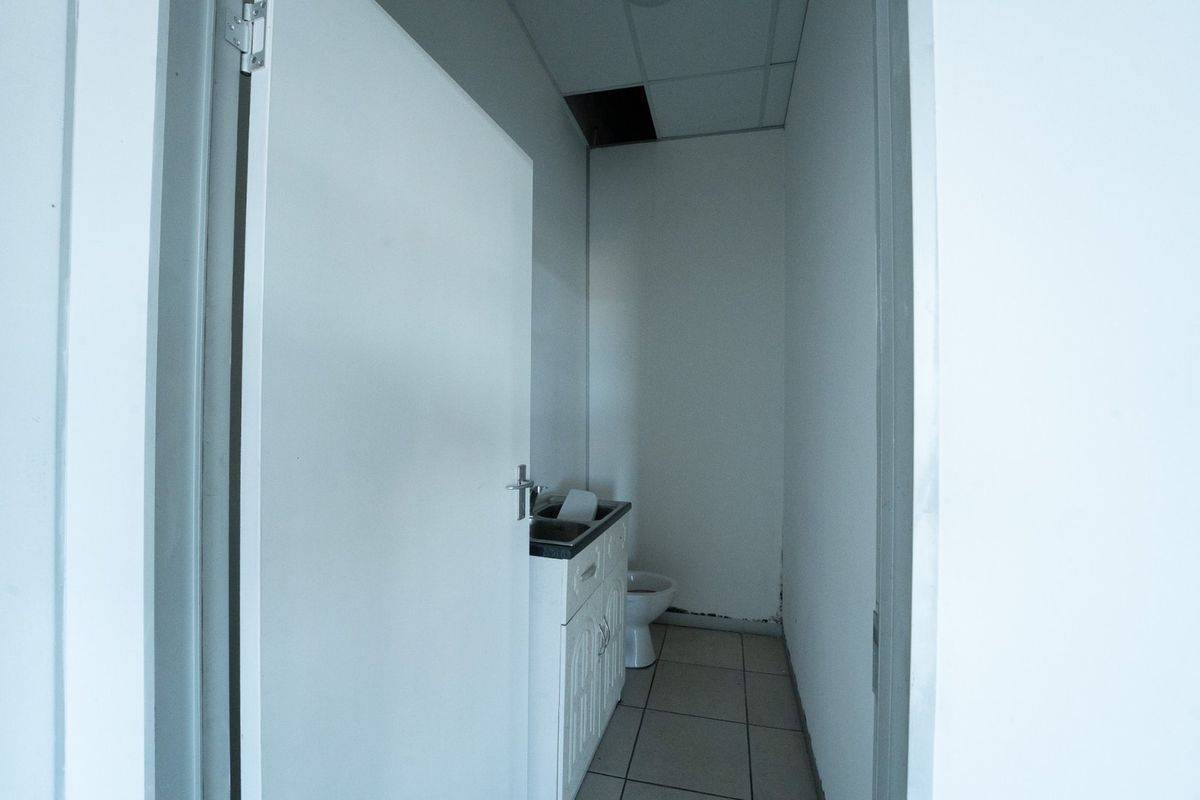 A small, basic bathroom featuring a vanity with sink, a toilet, tiled flooring, and a drop ceiling with a missing panel.