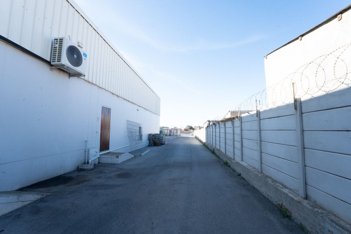 Rear exterior service area featuring an asphalt driveway, precast concrete boundary wall with razor wire, and an external air conditioning unit.