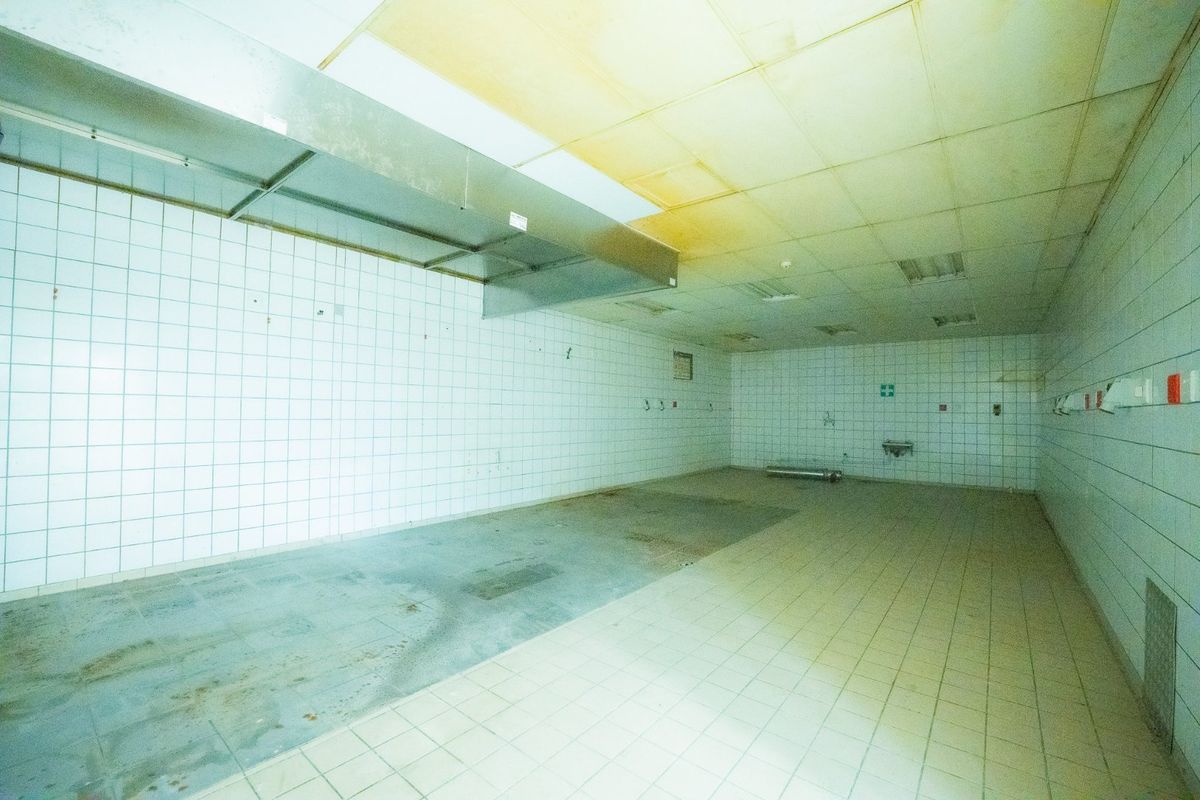 A large, empty commercial-style kitchen space featuring tiled walls, tiled flooring, and a stainless steel extractor hood, requiring significant refurbishment.