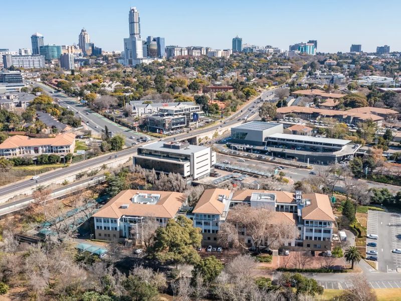 Aerial view of a commercial office complex featuring multiple buildings, tiled roofs, and extensive parking facilities within an urban setting.