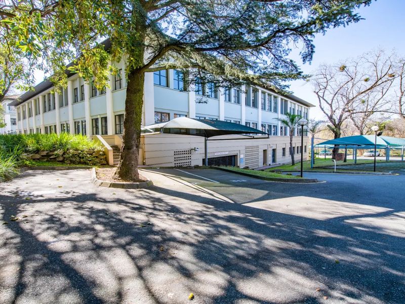 Exterior view of a multi-story commercial building featuring an asphalt driveway, covered parking area, and established landscaped surroundings.