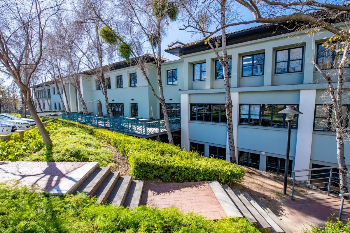 Rear view of a commercial building featuring a raised patio area, landscaped garden, and paved access stairs with multi-level architectural facade.