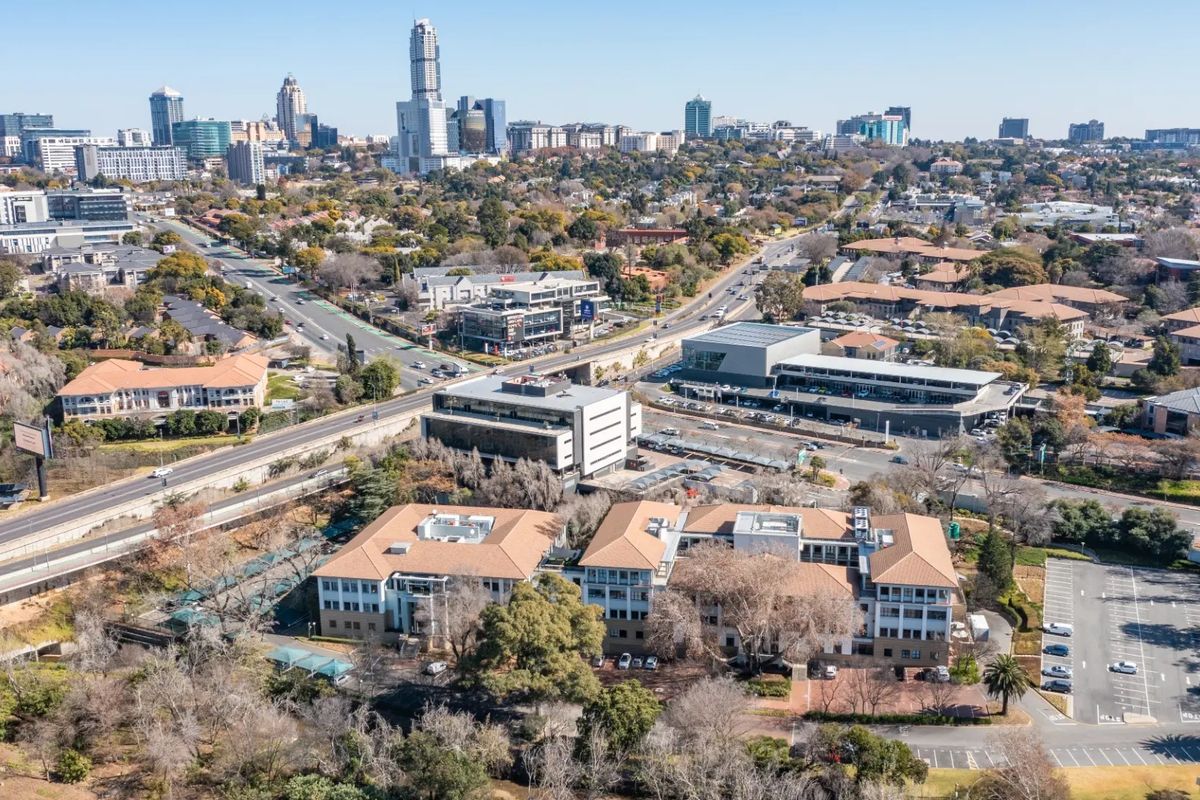 Aerial view of a commercial office complex featuring multiple buildings, tiled roofs, and extensive parking facilities within an urban setting.