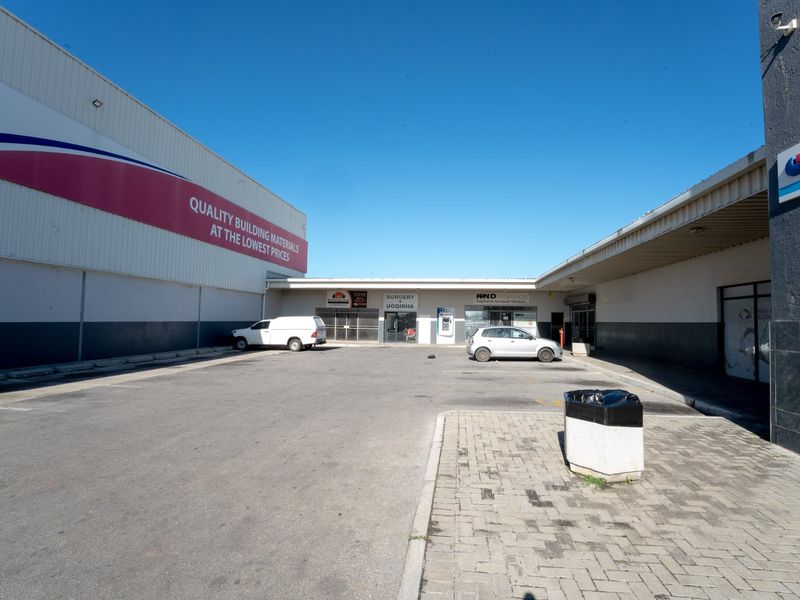 Front exterior view of a commercial retail complex featuring paved parking, metal cladding, and multiple storefront entrances.