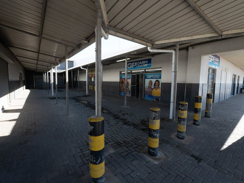 Commercial exterior front view featuring a covered walkway, paved access area, and shopfront entrance with security bollards and signage.
