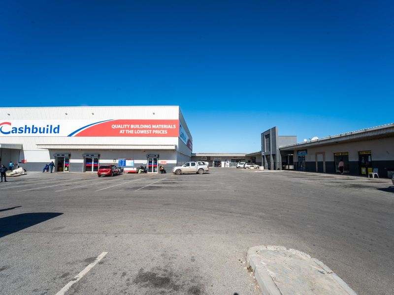 A wide-angle view of a commercial retail center featuring a large Cashbuild store with an expansive asphalt parking area.