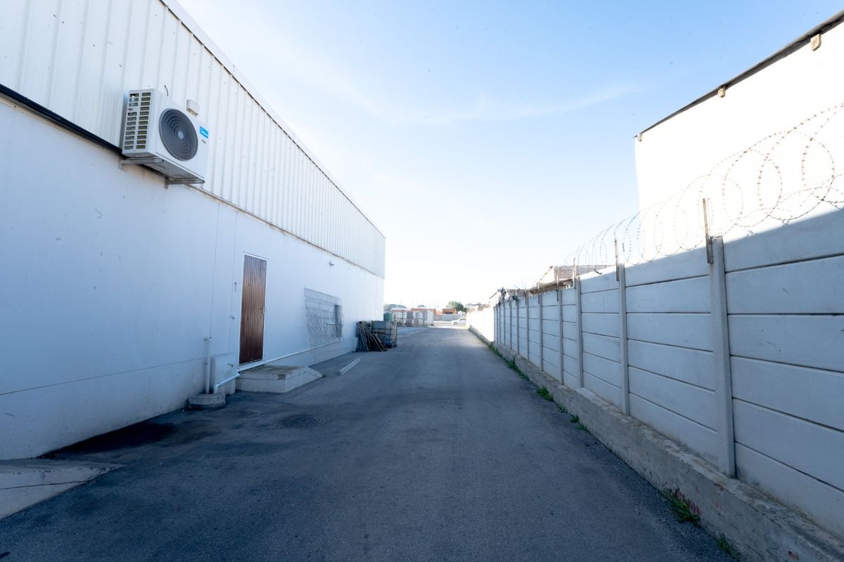 Rear exterior access area featuring an asphalt driveway, secure precast concrete boundary wall with razor wire, and wall-mounted air conditioning unit.