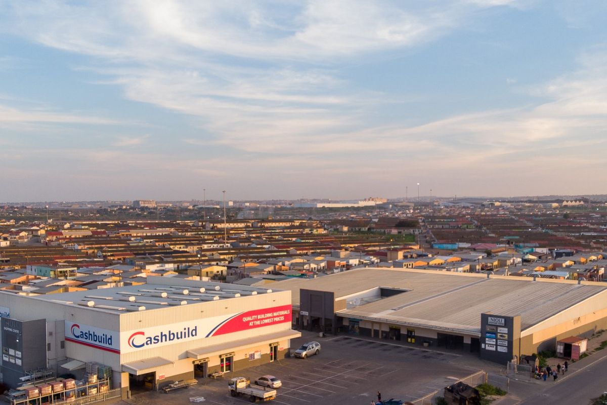 Aerial view of a commercial retail complex featuring large warehouse structures, paved parking areas, and prominent signage in a suburban setting.