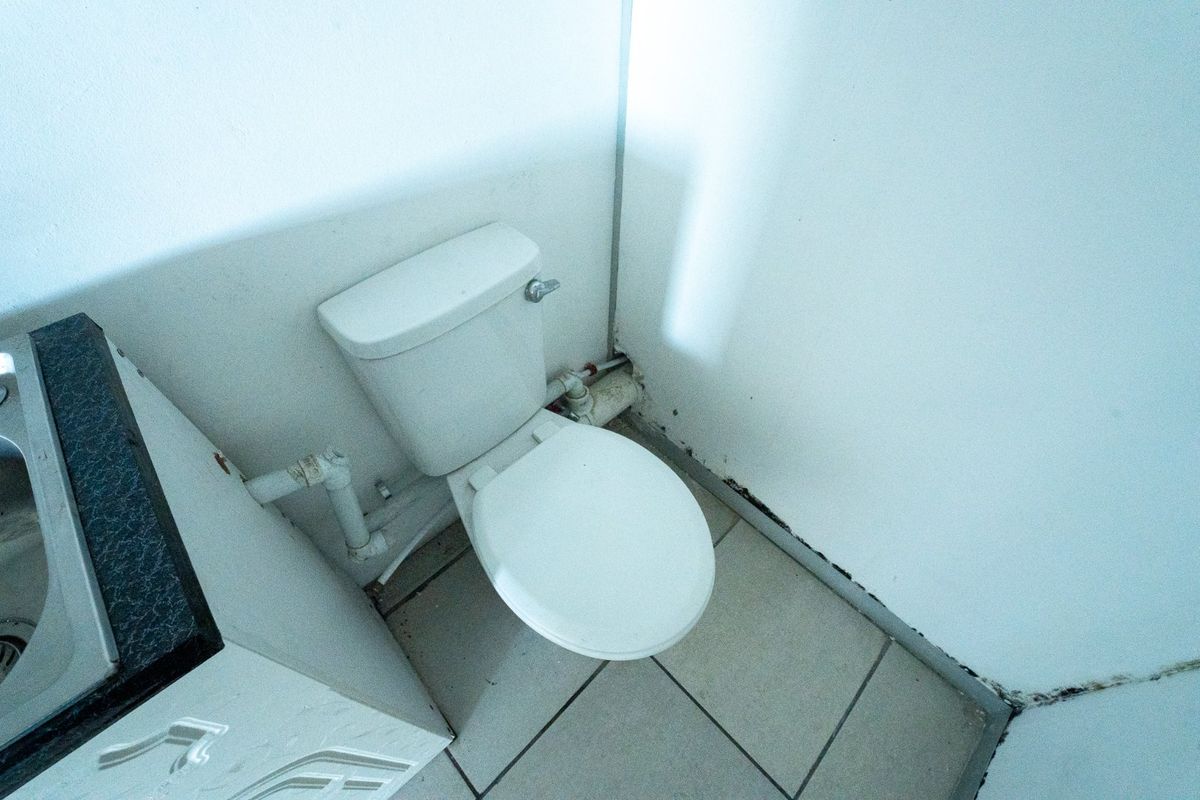 A small, dated bathroom featuring a standard toilet, vanity with sink, and tiled flooring, currently showing signs of wear and visible mold.