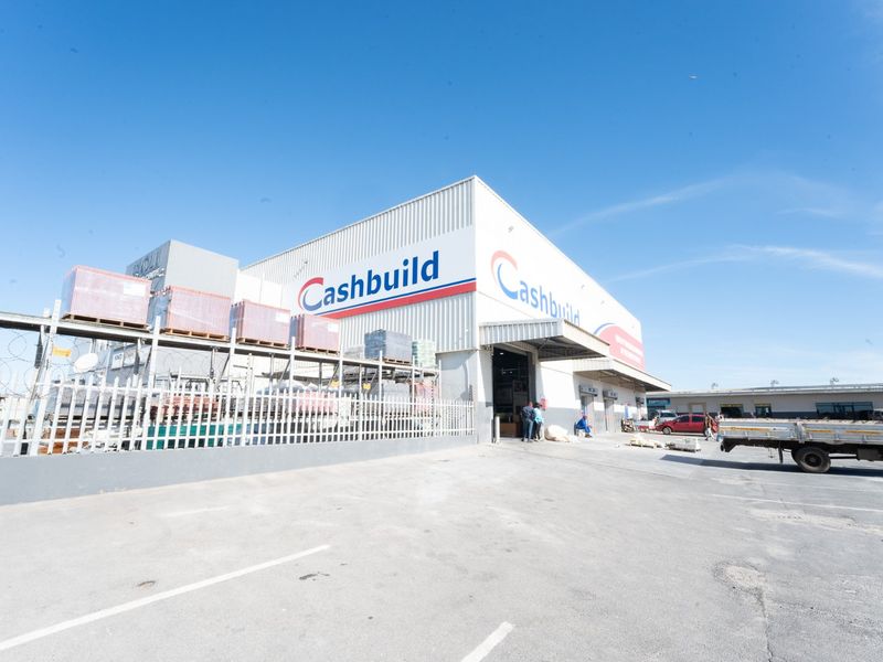 Exterior view of a commercial retail warehouse facility featuring metal cladding, a loading bay, and a paved parking area with security fencing.