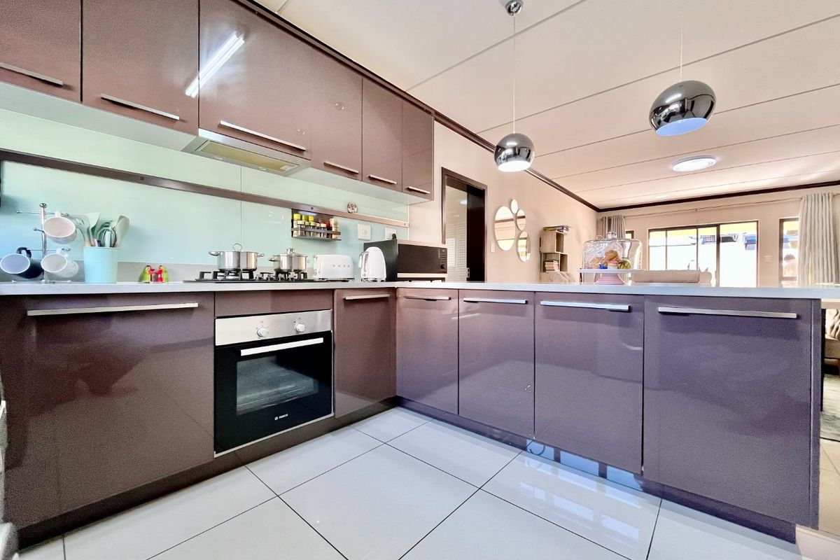 Modern open-plan kitchen featuring high-gloss cabinetry, integrated appliances, sleek glass splashback, and large format floor tiles, flowing into the adjacent living area.