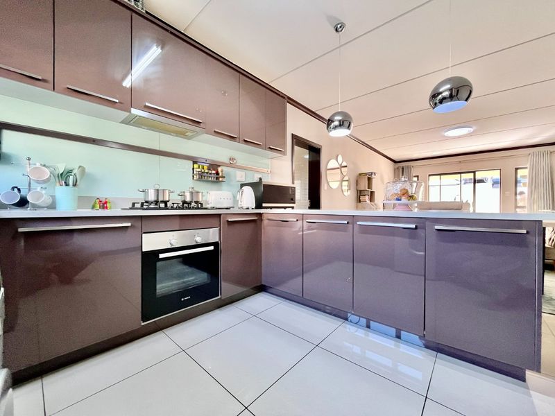 Modern open-plan kitchen featuring high-gloss cabinetry, integrated appliances, sleek glass splashback, and large format floor tiles, flowing into the adjacent living area.