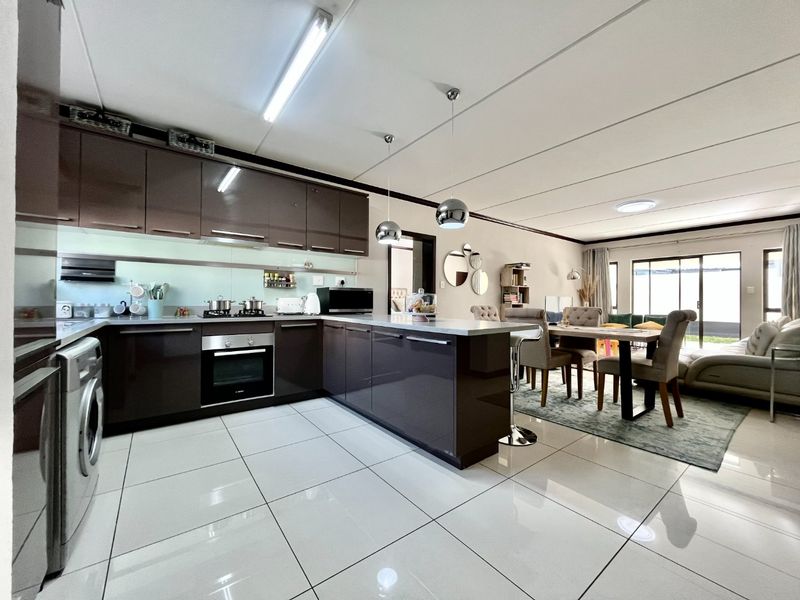 Modern open-plan kitchen and living area featuring high-gloss cabinetry, integrated appliances, tiled flooring, and seamless access to the outdoor space.