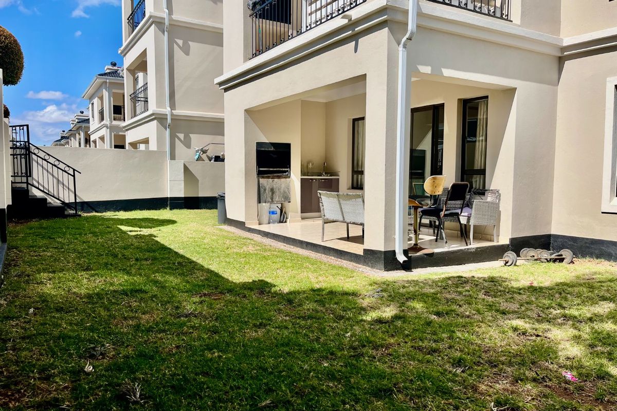 Rear view of the apartment featuring a covered patio with a built-in braai, tiled flooring, and access to a private garden area.