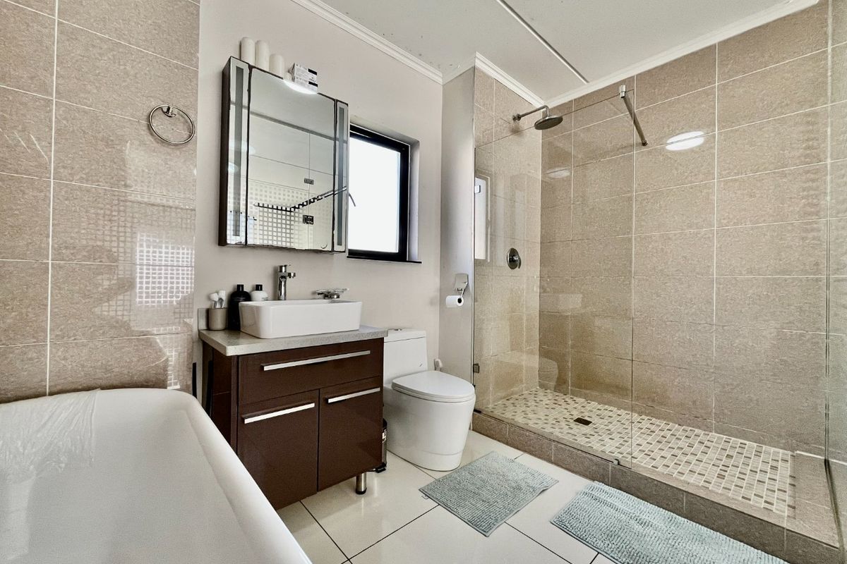 Modern bathroom featuring a walk-in shower with glass screen, a freestanding bathtub, a vessel sink vanity, and neutral floor-to-ceiling wall tiles.