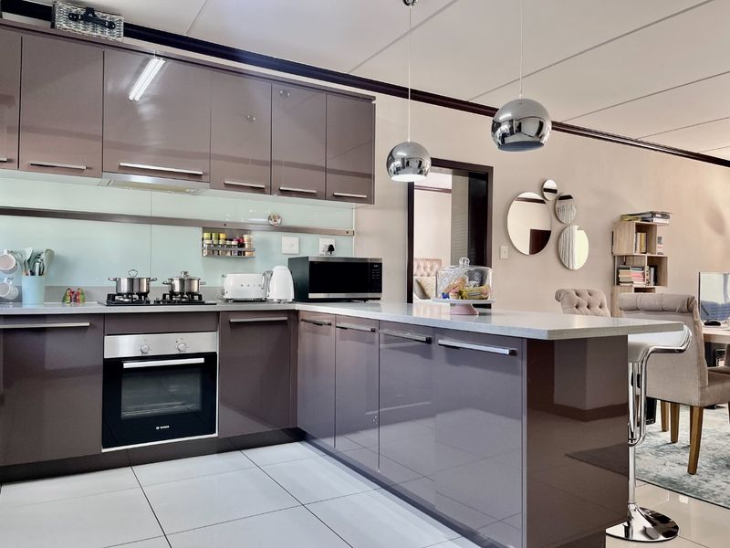 Modern open-plan kitchen featuring high-gloss cabinetry, stone countertops, integrated appliances, and stylish pendant lighting, seamlessly flowing into the adjacent living area.