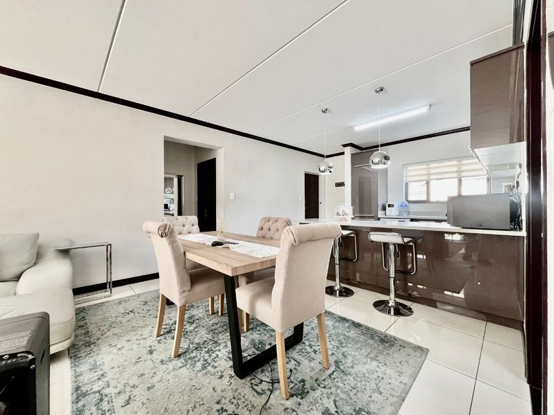 Modern open-plan living and dining area featuring a sleek kitchen with a breakfast island, glossy cabinetry, and neutral tiled flooring throughout.