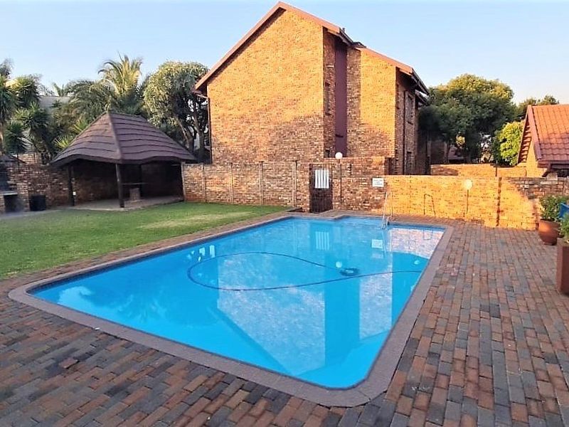 Communal pool area featuring a swimming pool, brick paving, a thatched gazebo, and a built-in braai facility within a secure brick-walled complex.