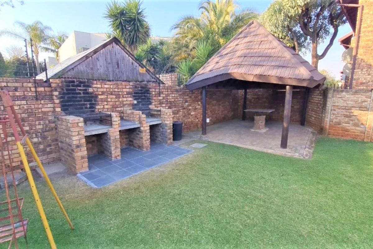 Rear garden area featuring a built-in brick braai, a thatched lapa with paved flooring, and a well-maintained lawn.