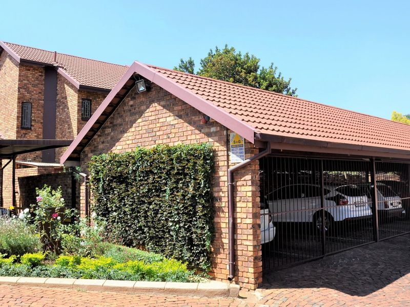 A well-maintained brick apartment complex featuring a covered parking area with security gates and paved driveway access.
