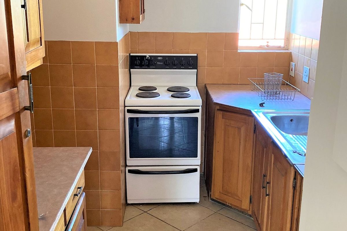 A functional kitchen featuring wooden cabinetry, a freestanding stove, tiled splashbacks, and a stainless steel sink with natural light from the window.