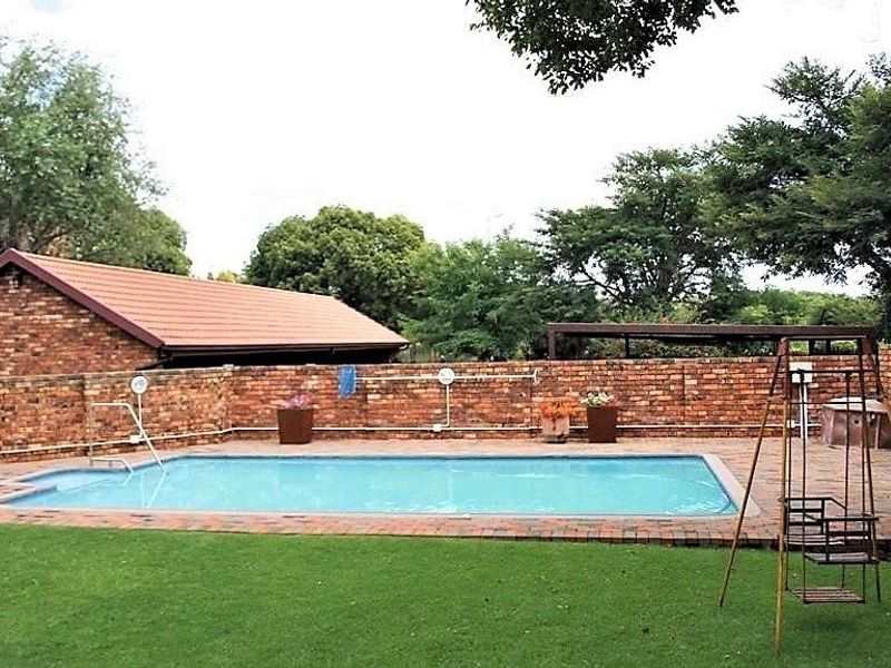 Outdoor pool area featuring a rectangular swimming pool, brick paving, and a surrounding brick boundary wall set within a garden space.