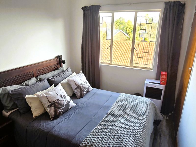 A cozy bedroom featuring a window with security bars and built-in cupboard storage, offering a functional and comfortable living space.