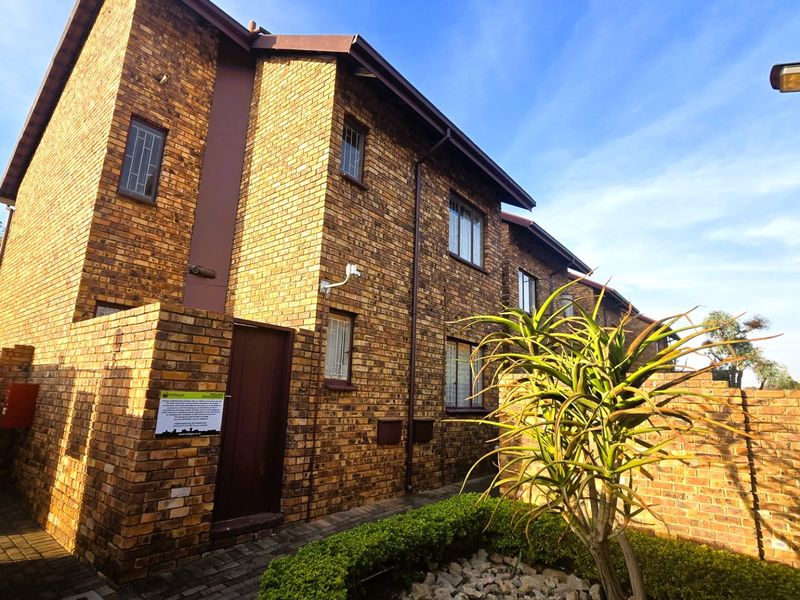 A well-maintained face brick apartment building exterior featuring secure windows, paved pathways, and established garden landscaping.