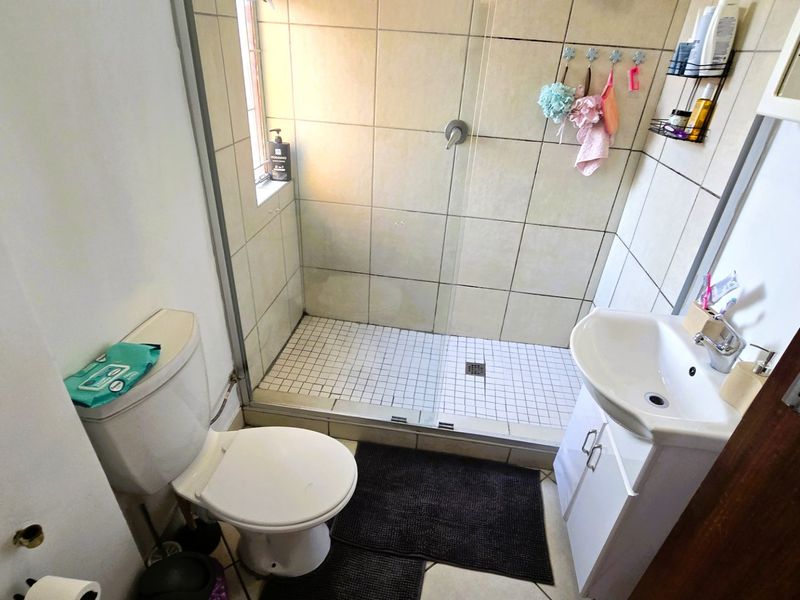 Compact bathroom featuring a walk-in shower with tiled walls, a vanity basin, and a standard toilet.