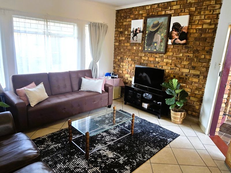 A living room featuring a prominent exposed brick feature wall, tiled flooring, and natural light from a large window.
