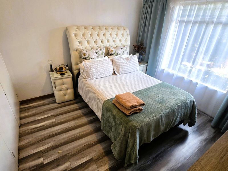A well-maintained bedroom featuring modern laminate flooring, a built-in wardrobe, and large windows with curtains allowing for natural light.