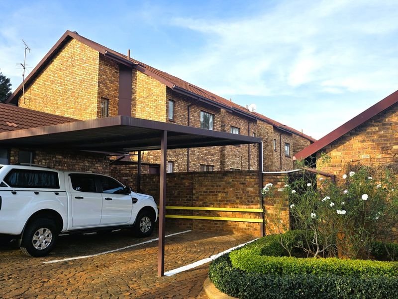 Exterior view of the apartment complex featuring face brick architecture, a covered carport, and a neatly landscaped garden area.