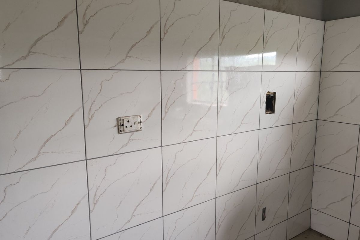 A kitchen wall featuring marble-effect ceramic tiling with unfinished electrical points and exposed plasterwork at the ceiling line.
