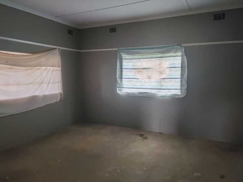 An empty bedroom featuring grey walls, concrete flooring, and ceiling ventilation grilles, requiring cosmetic updates to improve its overall condition.