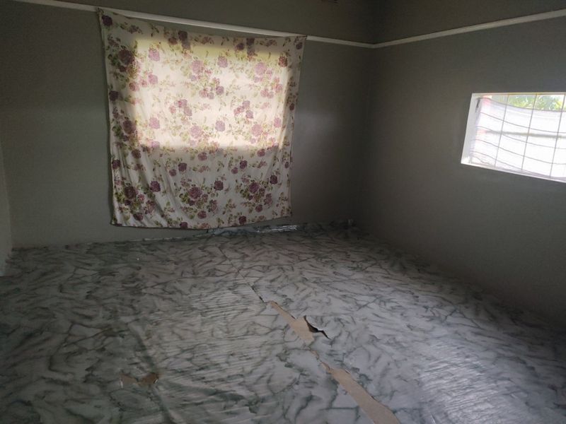 An empty bedroom featuring grey walls, a picture rail, and damaged flooring in need of replacement.