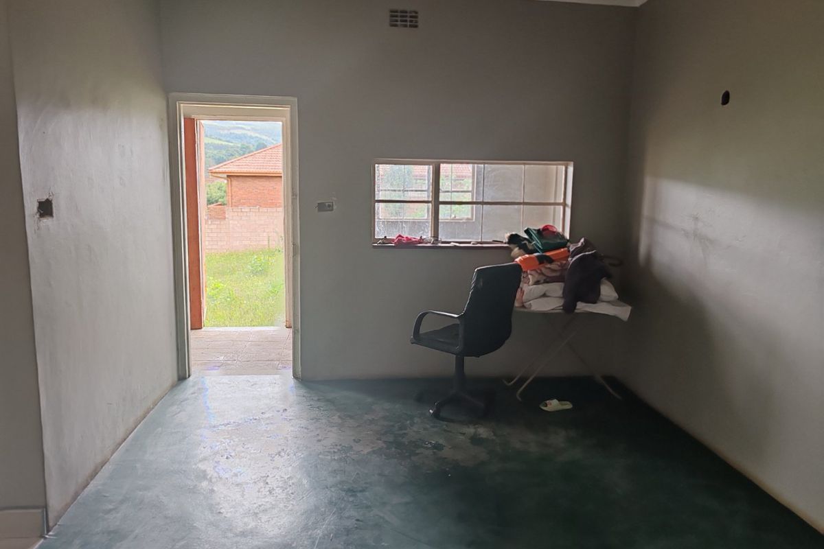 A simple, vacant bedroom featuring a steel-framed window, ventilation grille, and painted concrete flooring, offering a blank canvas for renovation.