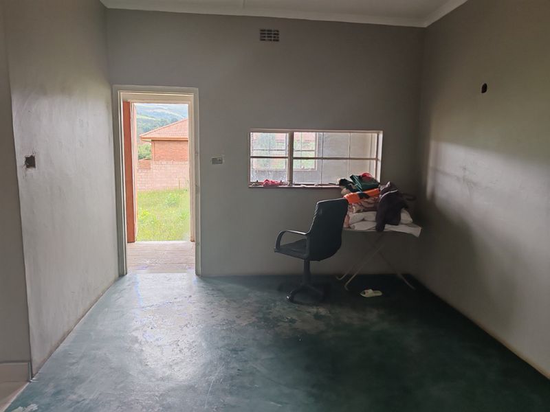 A simple, vacant bedroom featuring a steel-framed window, ventilation grille, and painted concrete flooring, offering a blank canvas for renovation.