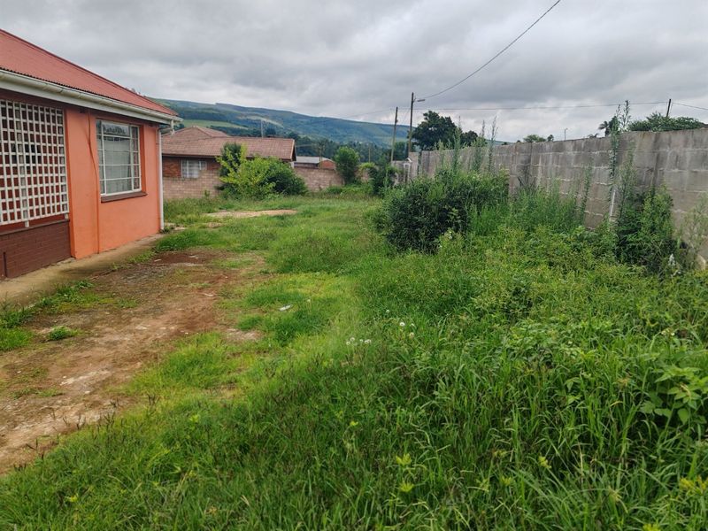 A rear exterior view of the property featuring a large, overgrown garden area enclosed by a concrete block boundary wall.