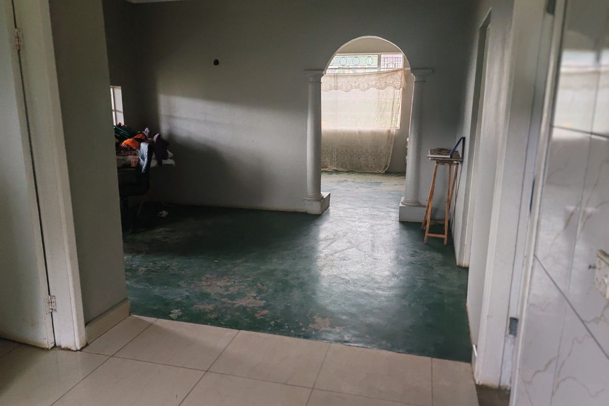 An empty living area featuring an arched entryway with decorative columns and worn flooring, offering a blank canvas for renovation and interior design updates.