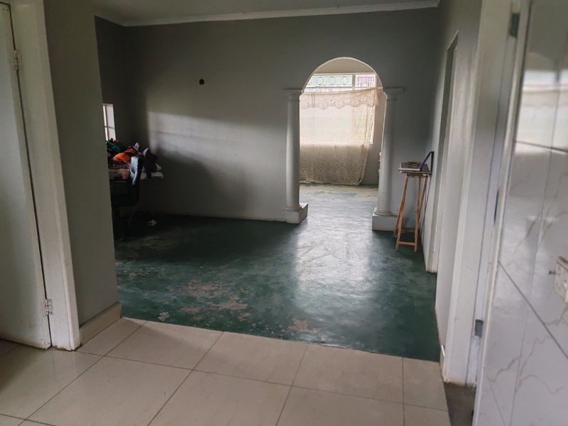An empty living area featuring an arched entryway with decorative columns and worn flooring, offering a blank canvas for renovation and interior design updates.