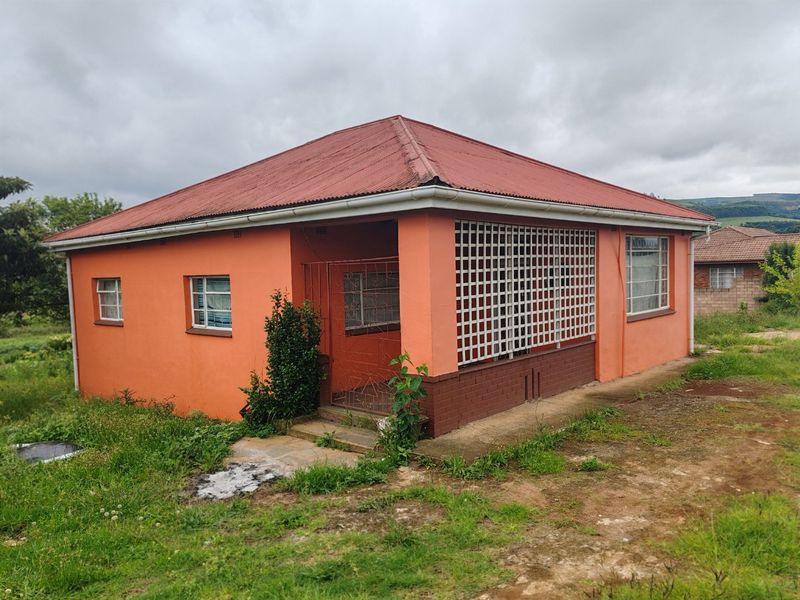 A detached single-story house featuring a corrugated metal roof, security bars on windows, and a concrete apron, set on a grassed plot.