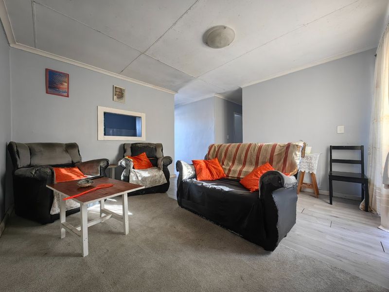 A living room featuring a mix of carpet and laminate flooring with visible ceiling panel wear, offering a functional space for renovation.